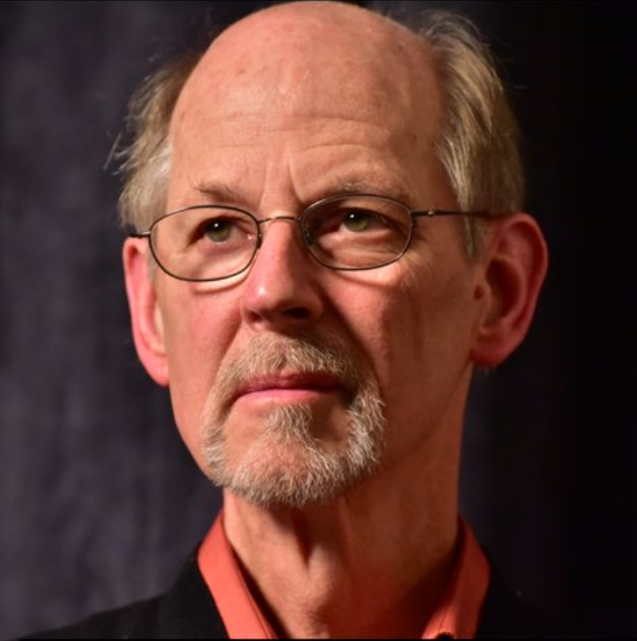 Marshall Vian Summers, grey-bearded and in wire-rimmed glasses, looking past the camera